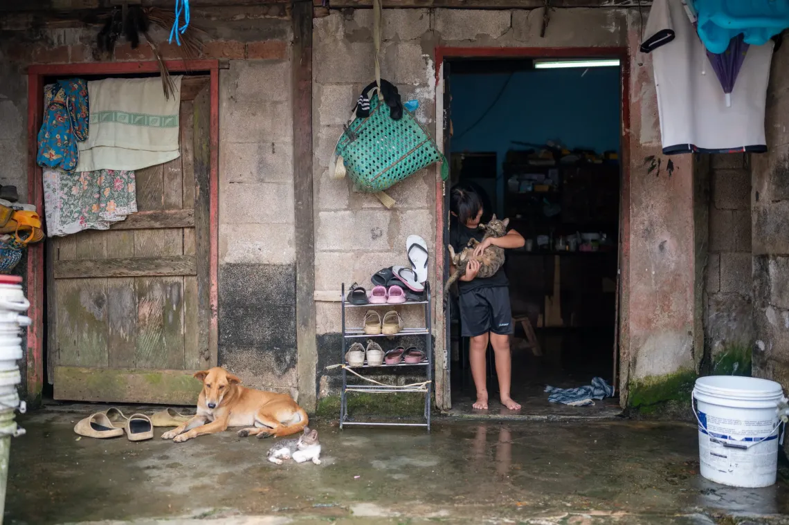 Zara stands in the doorway of her home holding a cat, with a dog and kitten resting outside.