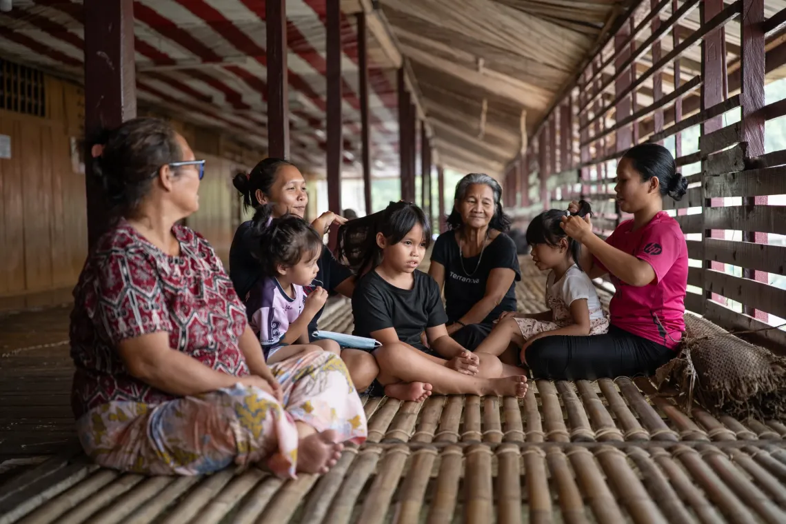 Zara sits with her family on the bamboo floor of a longhouse in Serian, Sarawak, as her mom braid the children&rsquo;s hair.
