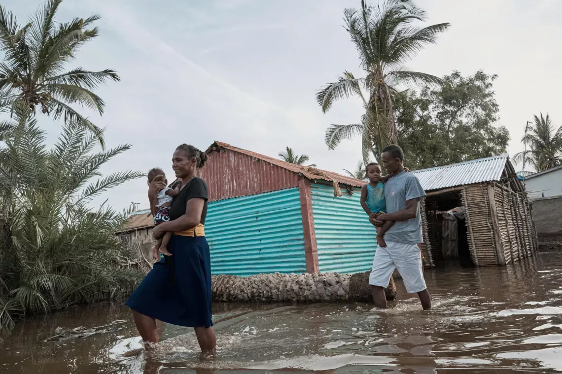 A family crossing flooded roads, both parents holding a child in their arms