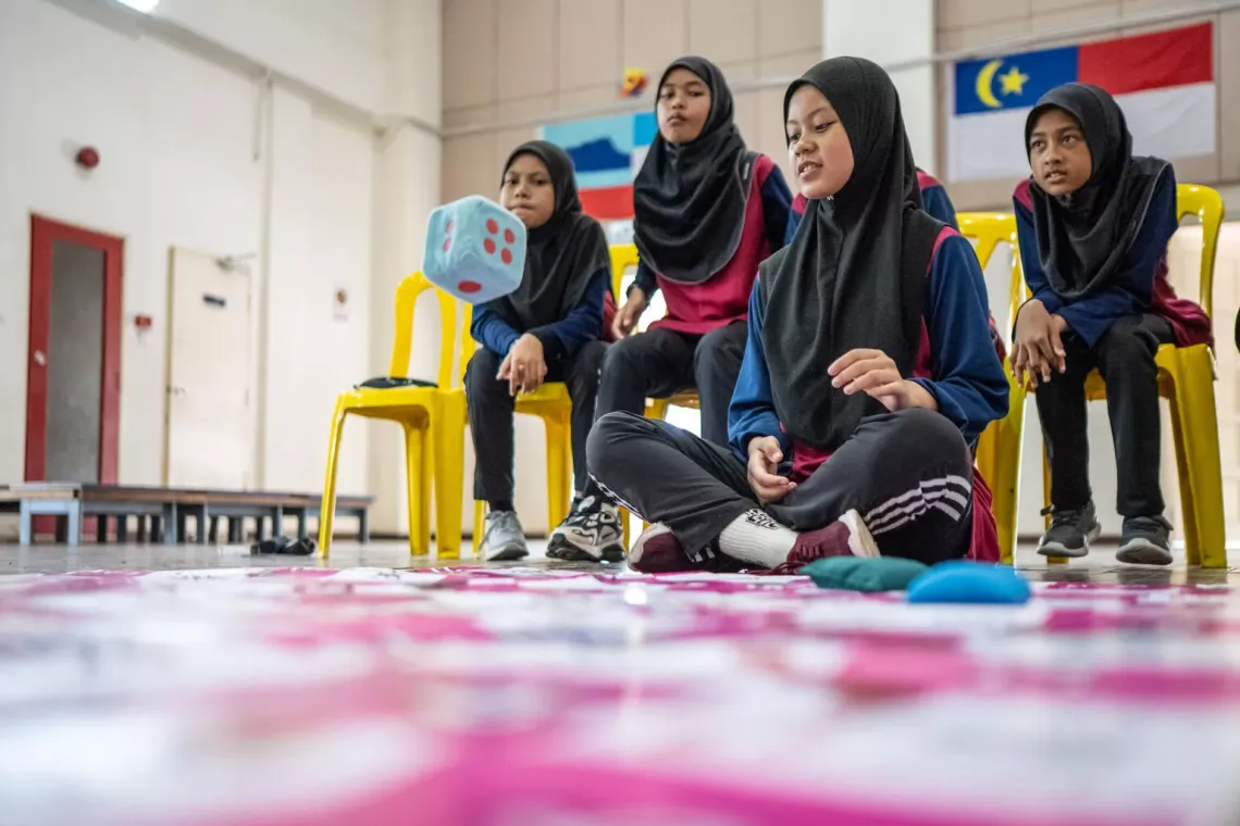 Students playing the DRR Snake and Ladders game, a twist on the classic board game, with questions tailored to teach disaster risk reduction.