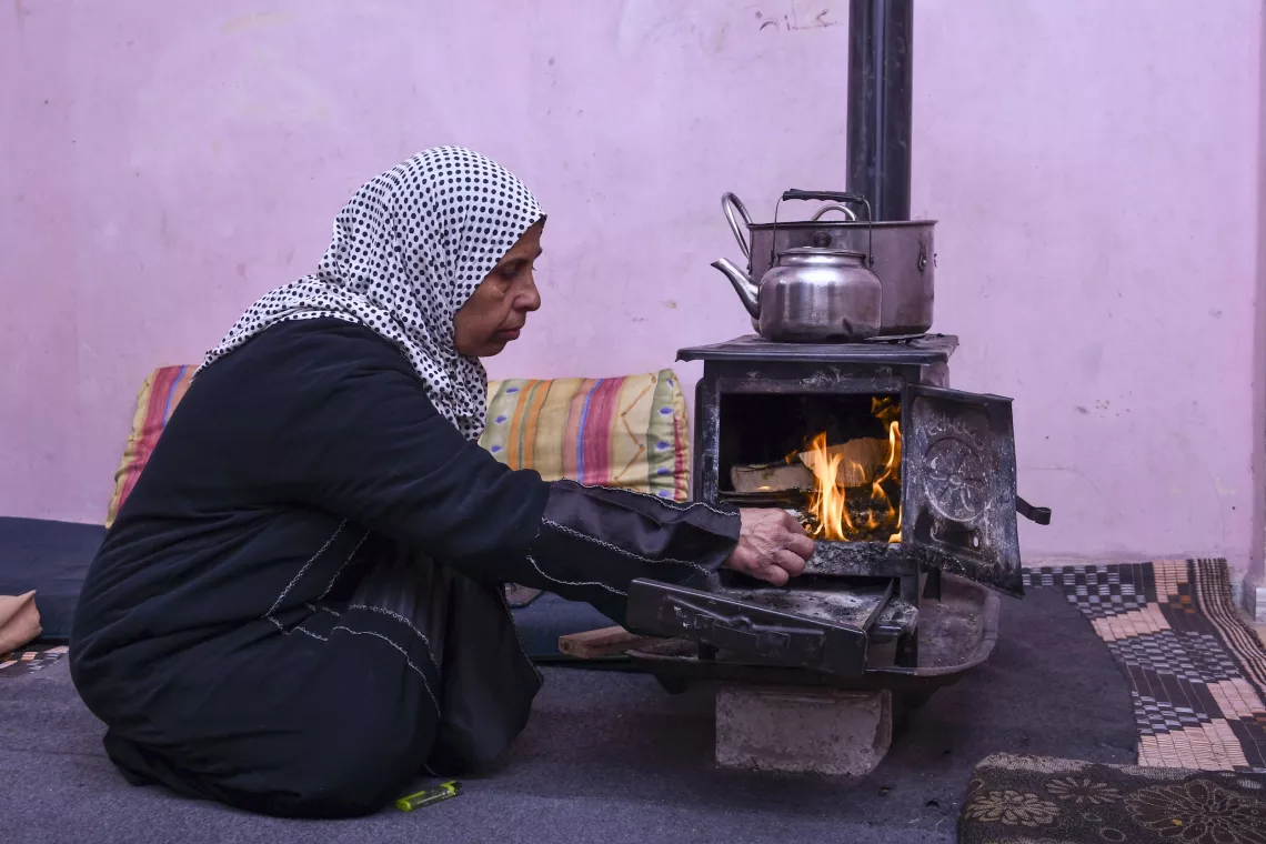 Farha, 45, tends to the wood stove in her apartment in Shabaa village, Rural Damascus.