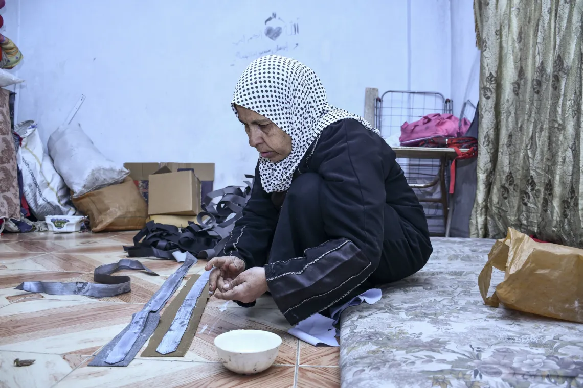 Farha, 45, sits cross-legged on a carpet in her apartment in Shabaa village, Rural Damascus, assembling belts .