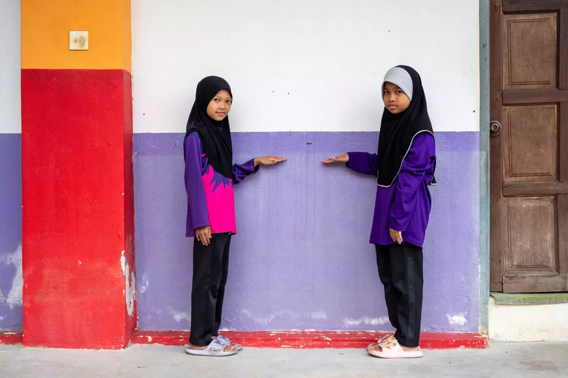 Two teen girls stand by a wall showing how high the water rises during flood