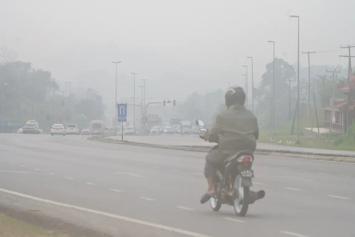 A motorcyclist travels along a road in Serian, Sarawak, as thick haze reduces visibility.
