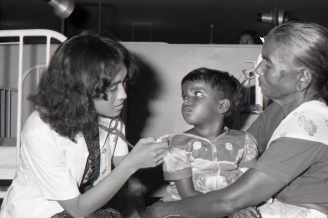 Child sits on mother's lap receiving vaccination from nurse.