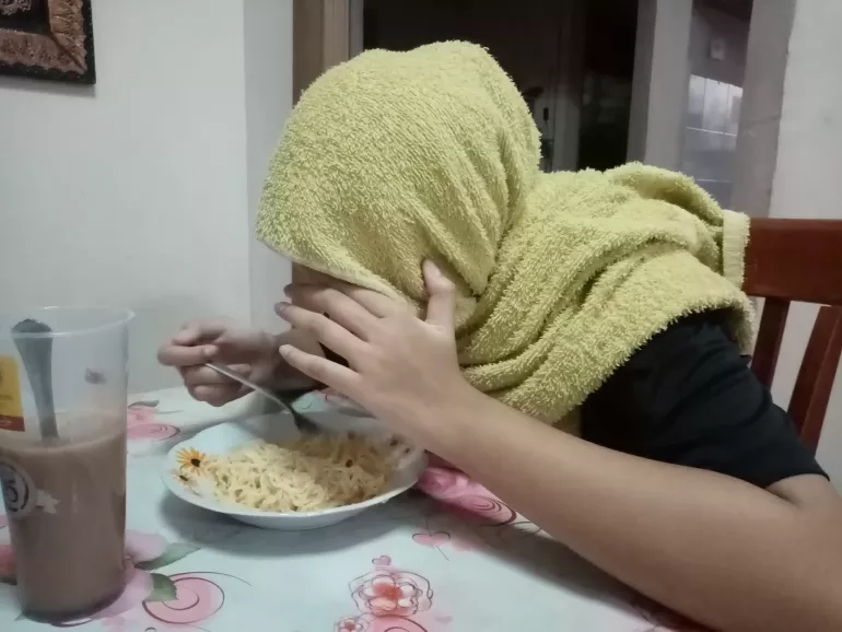 Woman hiding her face eating noodles