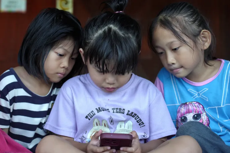 Three young girls stare at a phone screen