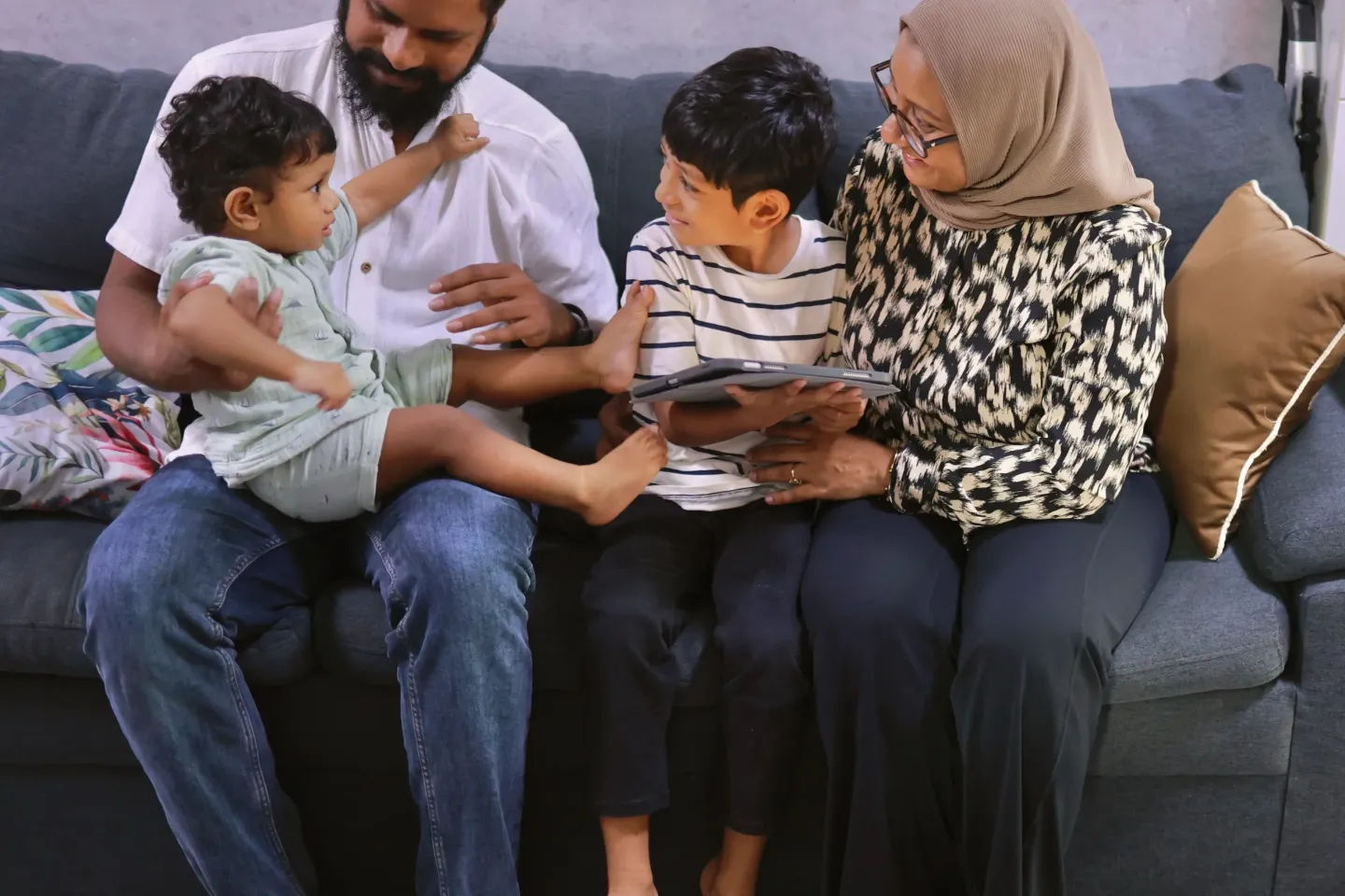 A family together on the sofa, one kid playing on an iPad 
