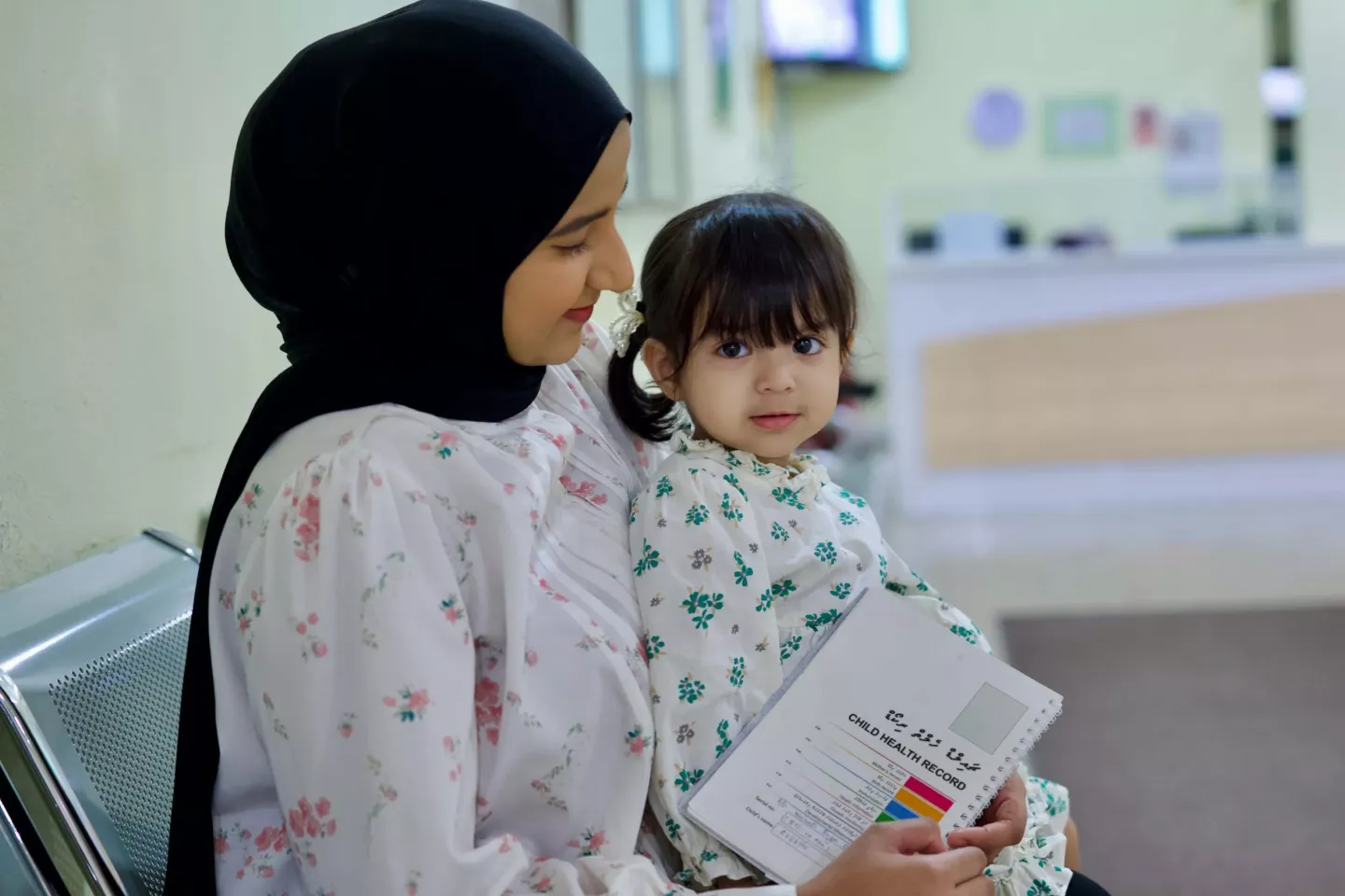 A mother holding her young daughter with her vaccination card