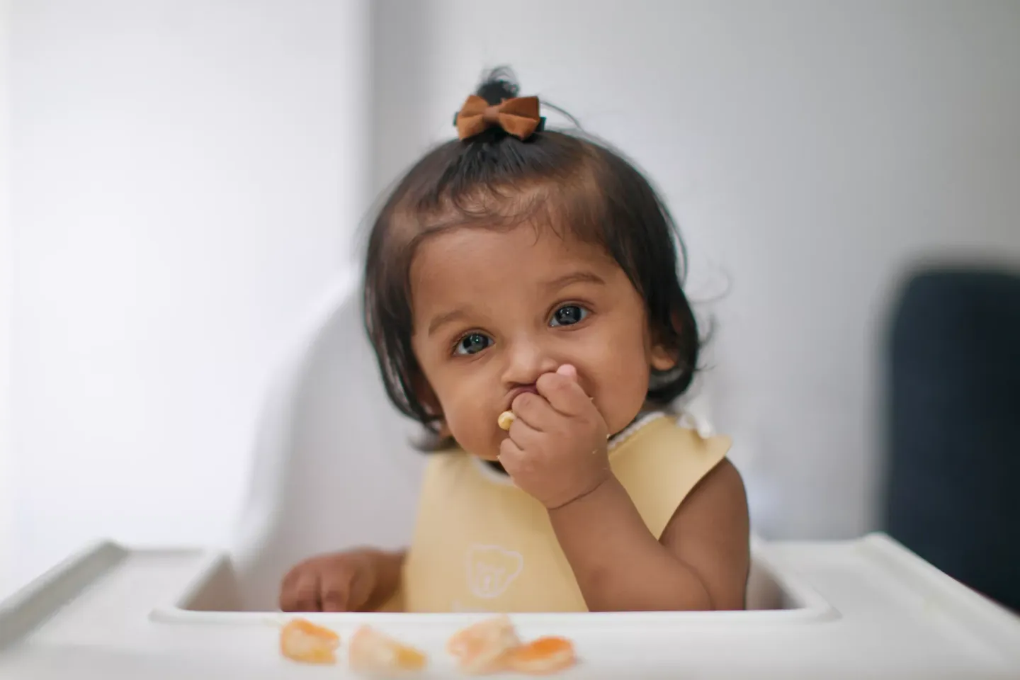 A baby girl eating pieces of an orange, while looking at the camera