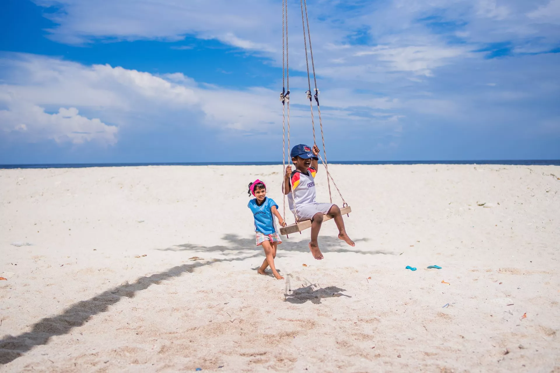 Two children play on a swing on the beach.