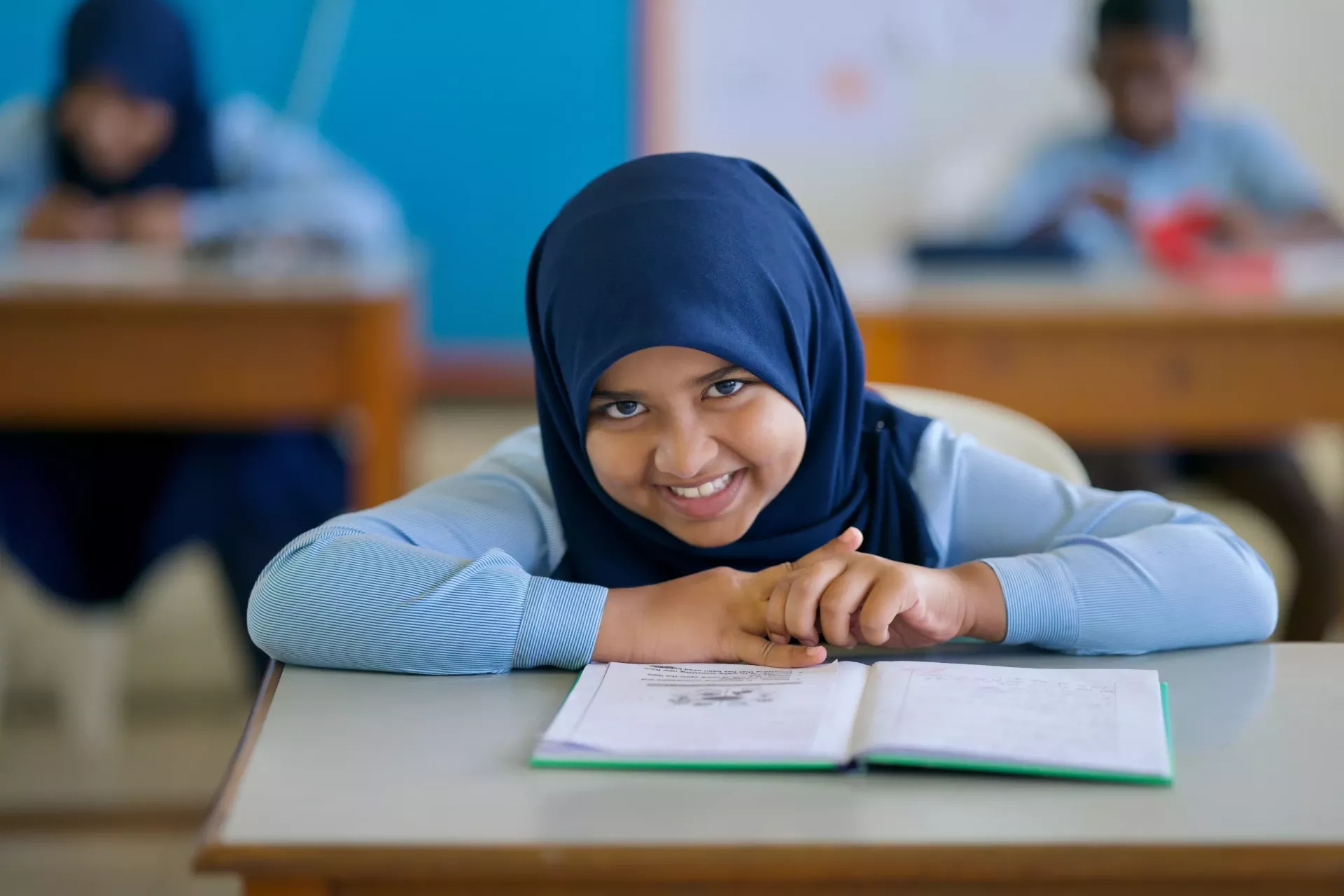 A young girl in school with a book in front of her. 