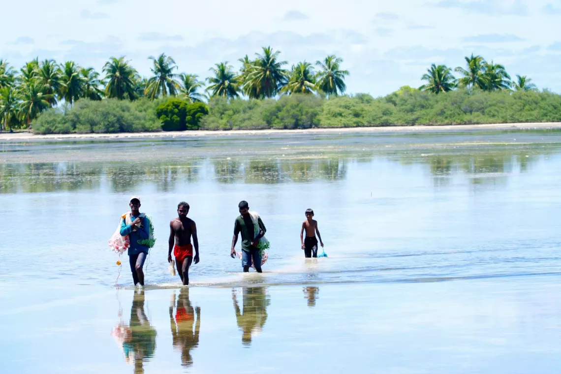 A group of men and boys fish in a lagoon.
