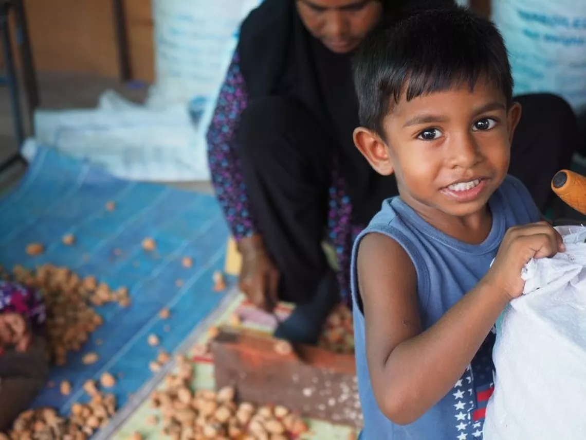 A young boy smiles at the camera while helping his family prepare food.