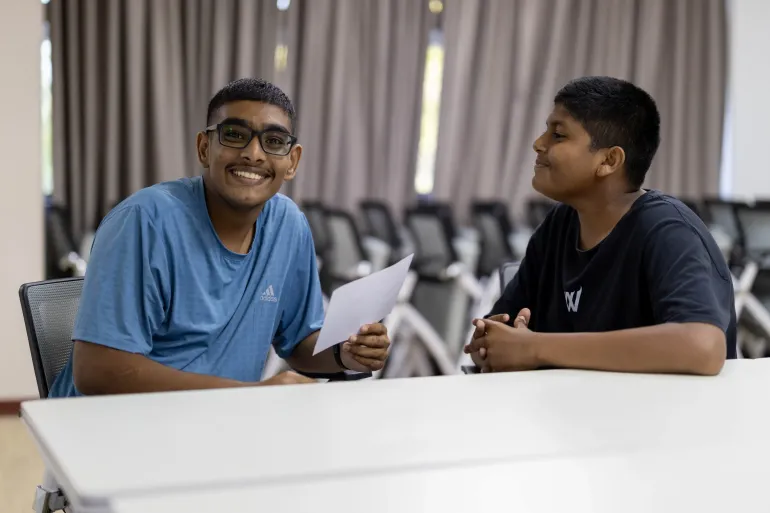 Two boys conversing together, one is looking at the camera