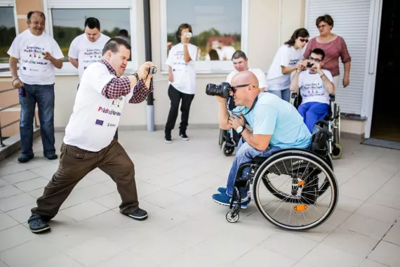 A photographer with disabilities takes a photograph of another photographer with disabilities.