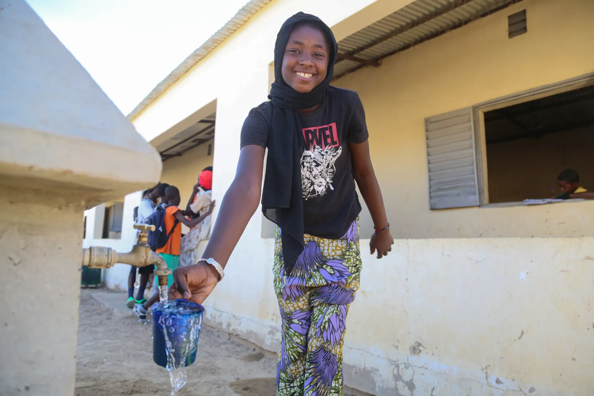 Souriante, Awa Yattara, 12 ans, &eacute;l&egrave;ve de 8ᵉ ann&eacute;e, remplit son bol d&rsquo;eau fra&icirc;che &agrave; la borne fontaine pour se d&eacute;salt&eacute;rer.