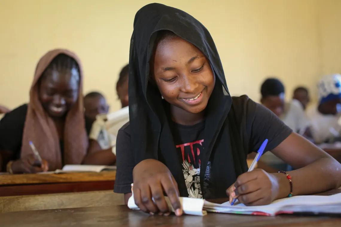 Awa, 12 years old and an 8th grade student, is seated in class, focused on her notebook as she writes attentively.