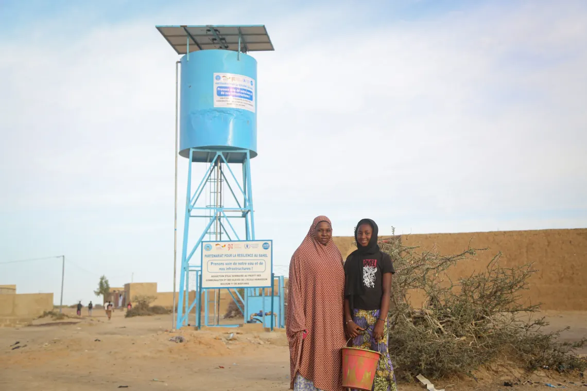 Mrs. Fatouma Ascofar&eacute; and her daughter Awa in front of the solar-powered borehole equipped with a basic water supply system installed in their village.