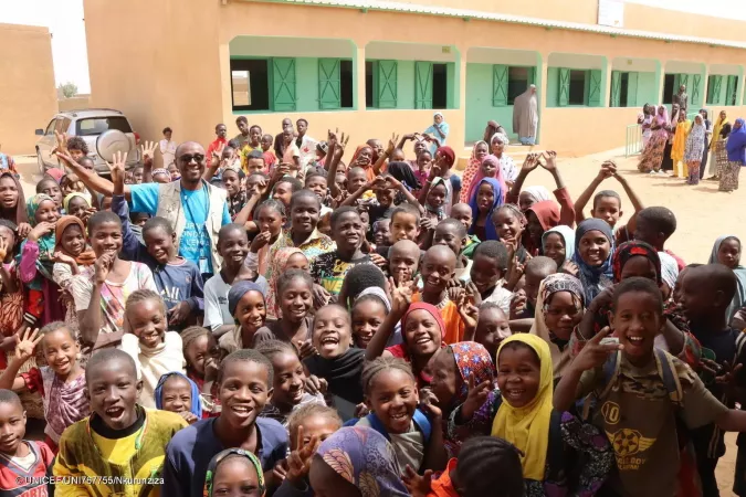 Un groupe d'environ 30 enfants saluent et sourient devant un nouveau b&acirc;timent scolaire.