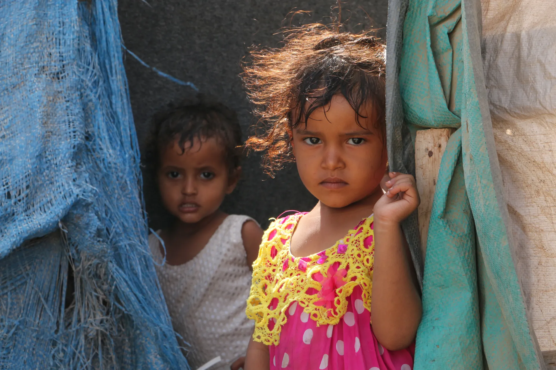 Two children looking from behind their tent drapes