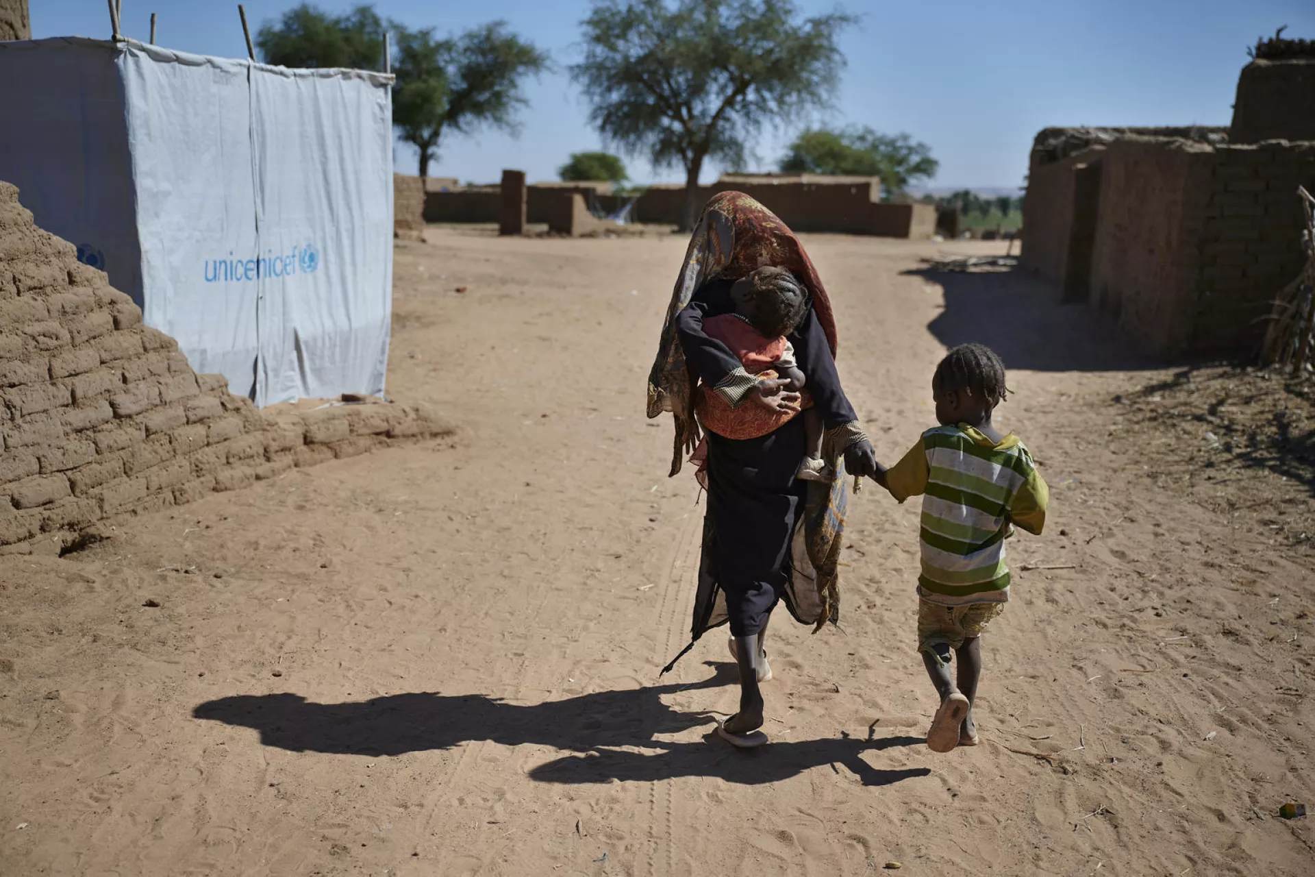 girl walking while carrying a baby and holding a little kids hand