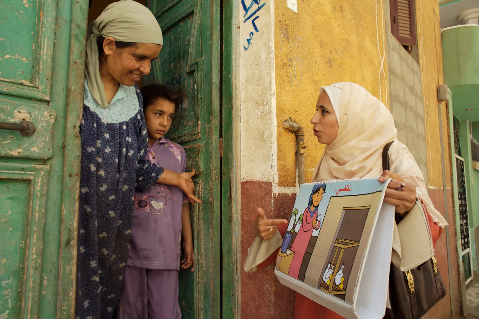 (Left-right) Saida Ali Suleuman and her daughter speak with Tahany El Zanfly in Masara Village, in Mit Ghamr District. Ms. Zanfly is a health worker conducting home visits to teach families how to prevent the spread of avian influenza from domestic poultry. [#5 IN SEQUENCE OF FIVE]