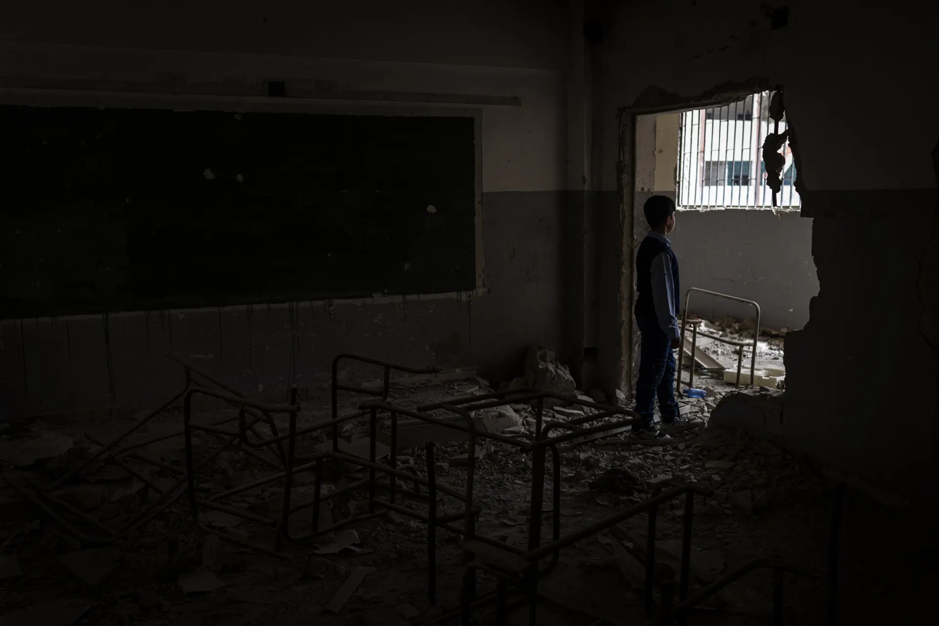 A boy looking out the window in a destroyed classroom