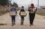 two boys carrying supply boxes and walking with their mother