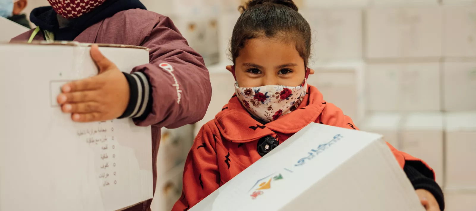 Lara, 4, wearing a mask and carrying her warm winter clothing kit from UNICEF.
