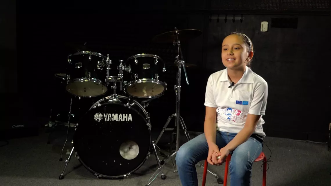 A girl sitting next to a drums set