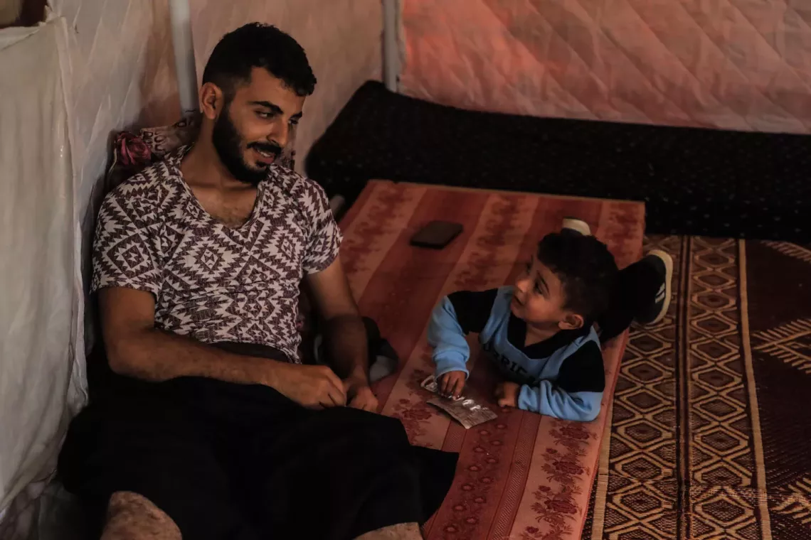 Gaza. Masoud sits on the floor with his son.