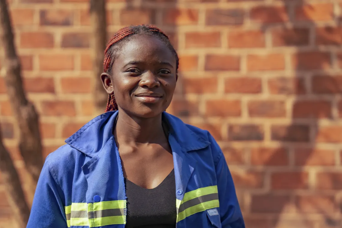 Astride poses outside for a portrait in her blue work jacket with a yellow safety stripe. 