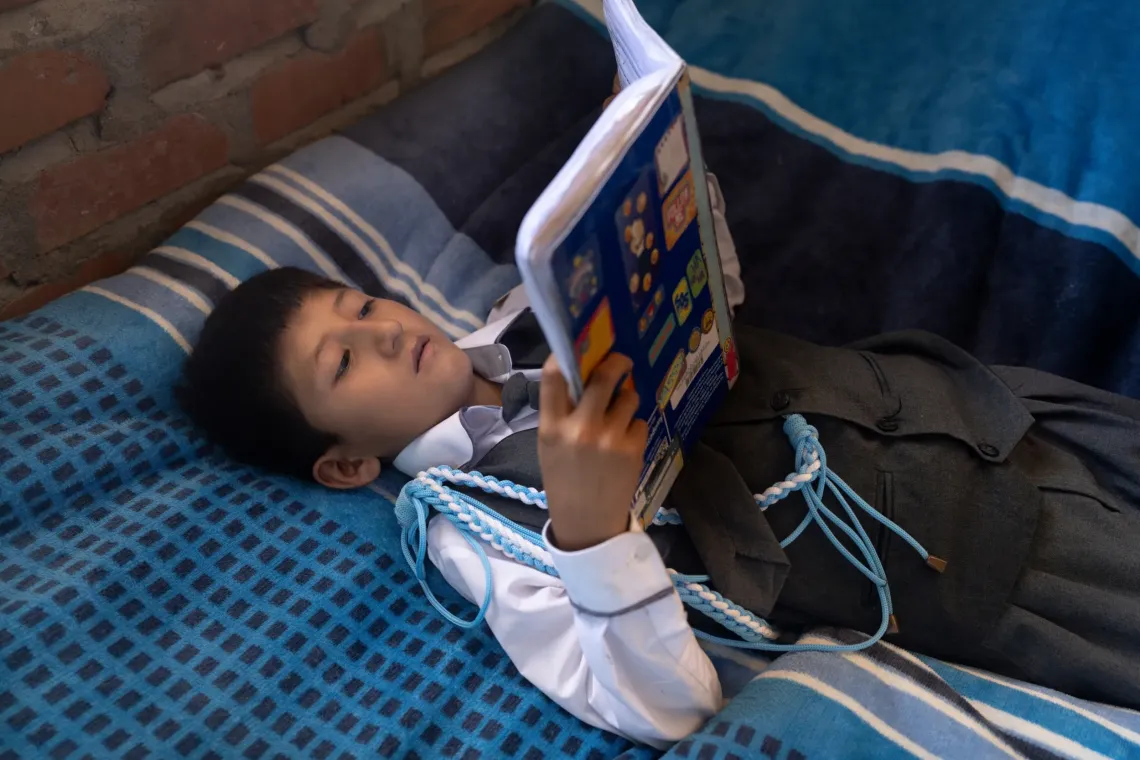 Hansel lies on his bed reading while dressed in his school uniform. 