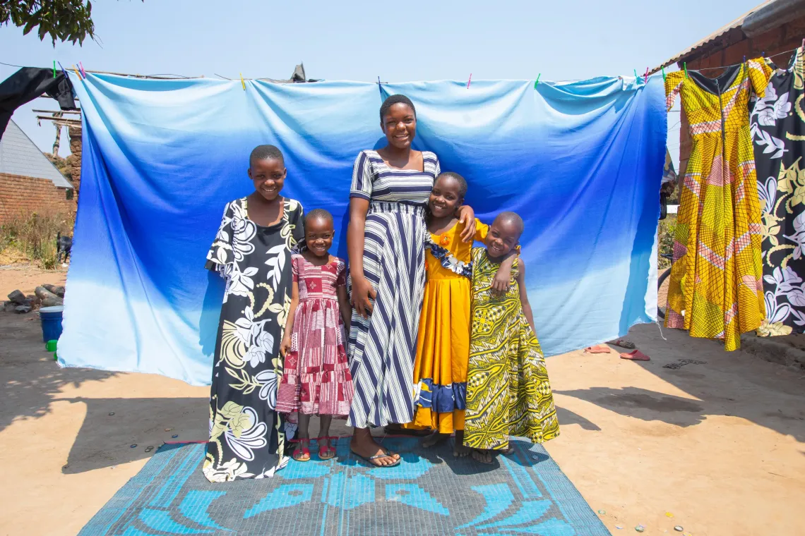 ntini stands with her four younger sisters, wearing bright dresses in front of a blue backdrop. 