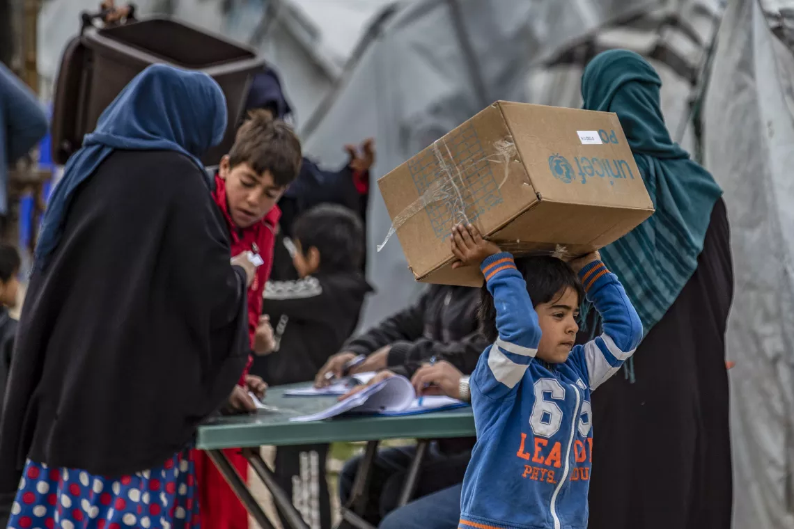 Children and families carry their newly received winter clothing kits, distributed by UNICEF in Roj camp, northeastern Syria.
