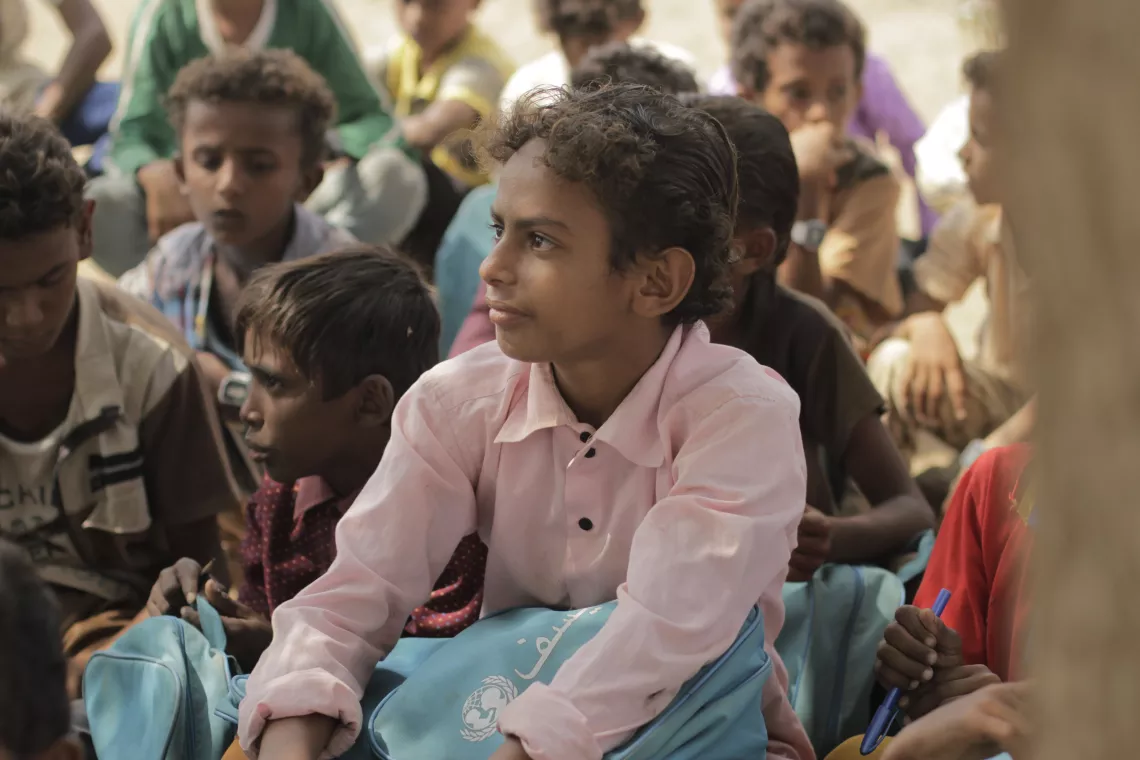 Young boy sitting on the ground at a school with his colleagues 