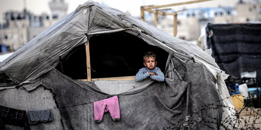 A child peers out from a makeshift shelter built from wood and plastic, where displaced families have sought safety in Rafah, south of the Gaza Strip.