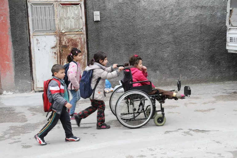A girl on a wheelchair with her siblings walking behind her