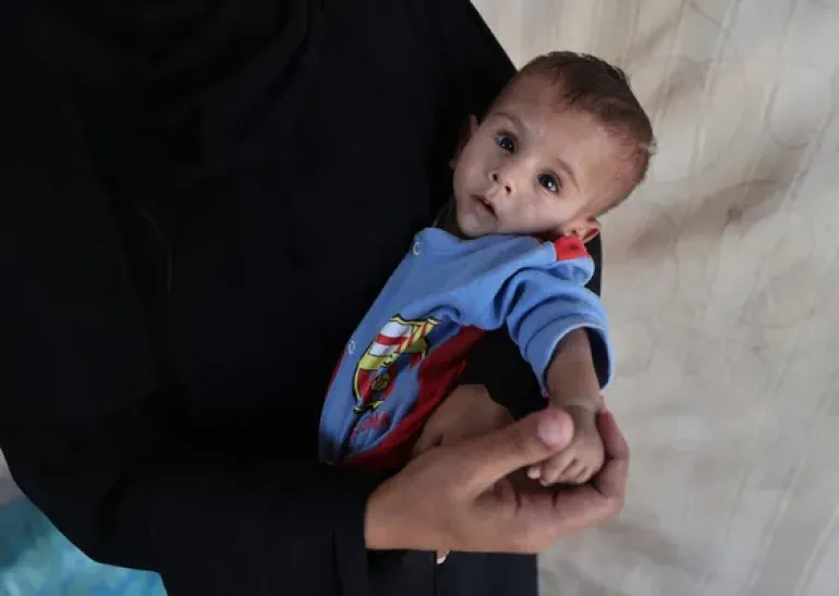 On 7 October 2025, Eitemad holds her son Ali in their makeshift tent in Al-Mawasi in the Gaza strip.
