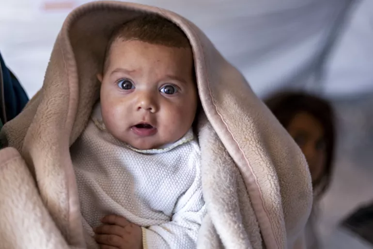 A baby held and wrapped in a blanket to keep warm in Winter. Alepo, Syria