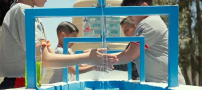 Ni&ntilde;os lavando sus manos en una toma de agua comunitaria de color azul al exterior de una escuela