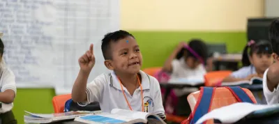 Ni&ntilde;o con uniforme escolar levanta la mano para participar en clase.