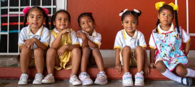 Cinco ni&ntilde;as con uniforme escolar sentadas en las escaleras de su escuela.