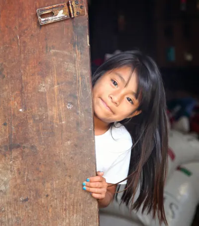 Una ni&ntilde;a se asoma sonriendo detr&aacute;s de una puerta de madera.