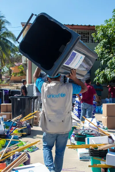Hombre con chaleco de UNICEF de espaldas a la c&aacute;mara, carga un bote que conten&iacute;a kits de emergencia que ya fueron entregados a quienes m&aacute;s los necesitaron durante una emergencia en Guerrero. 