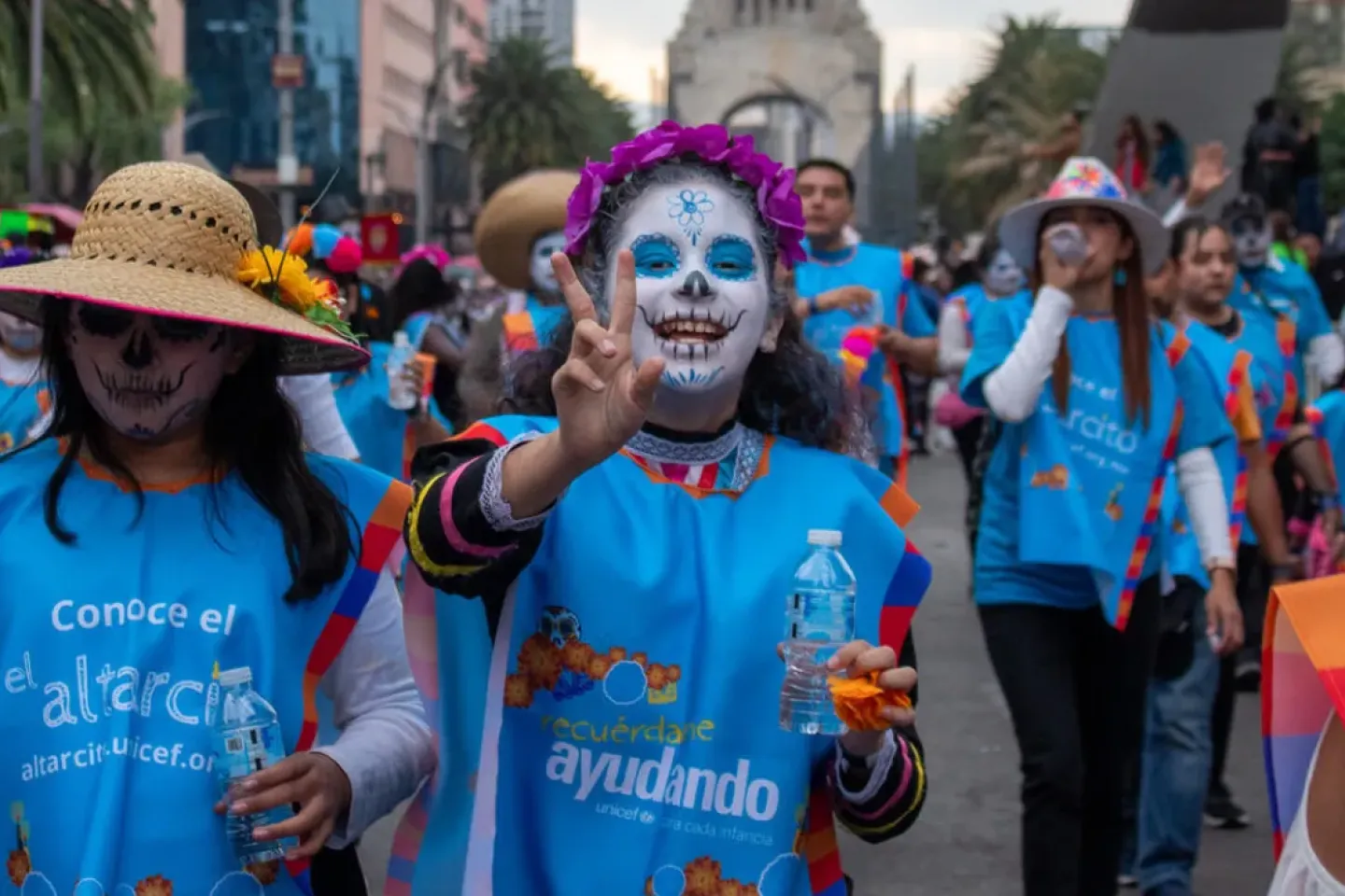 Grupo de j&oacute;venes con maquillaje de catrina y camisetas de UNICEF participan en un desfile de D&iacute;a de Muertos.