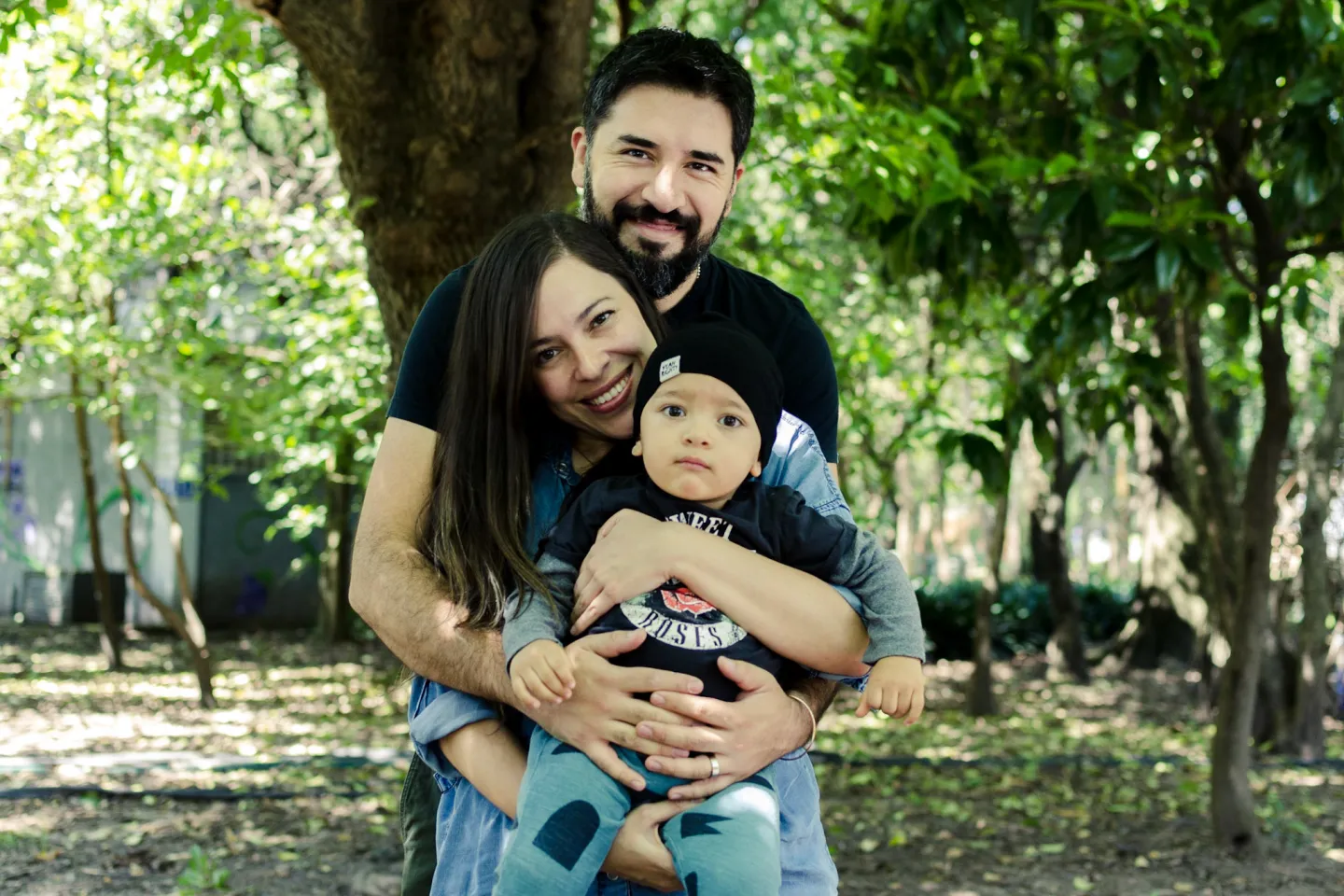Una madre y un padre cargan a su beb&eacute; en un parque; el v&iacute;nculo afectivo es la base de la crianza positiva.
