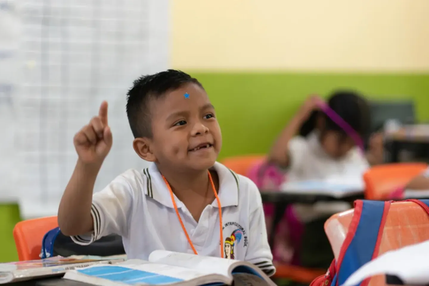 Ni&ntilde;o con uniforme escolar levanta la mano para participar en clase.