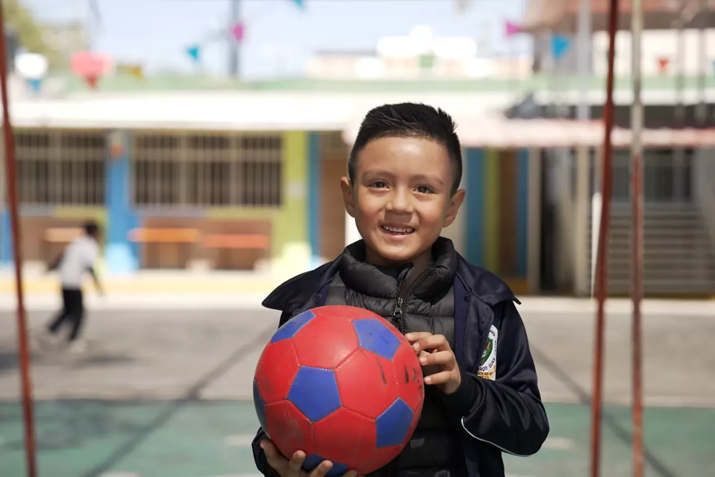 Mateo mira a la c&aacute;mara y sostiene un bal&oacute;n de futbol rojo